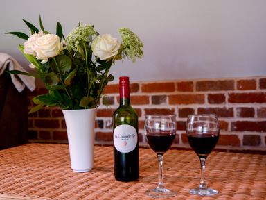 A table with a vase of white flowers red wine bottle and two glasses of red wine at Two Chantry Barns Orford
