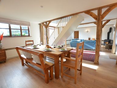 A dining area with wooden table and chairs next to a living room with blue sofas and a stove at Wheelwright's Barn in Walpole Near Halesworth