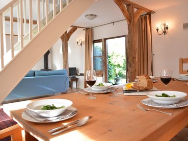 A dining table set with bowls of salad red wine glasses and sliced bread in a room with wooden beams and a blue sofa at Wheelwright's Barn Walpole Near Halesworth