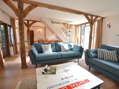 A living room with blue sofas wooden beams and a white staircase at Wheelwright's Barn Walpole Near Halesworth