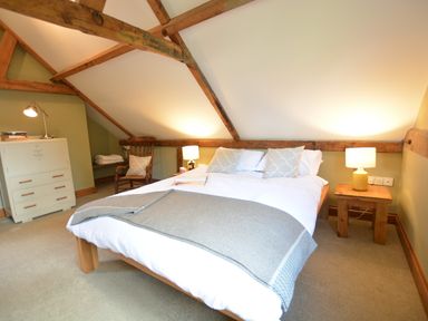A bedroom with a bed a wooden chair a cabinet and two bedside tables with lamps at Wheelwright's Barn Walpole Near Halesworth