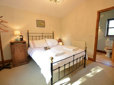 A bedroom with a double bed two folded towels on the bed a wooden nightstand with a lamp and cups and an en suite bathroom at Wheelwright's Barn in Walpole Near Halesworth