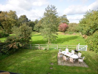 A backyard with an outdoor dining table and chairs near a wooden fence with trees beyond at Wheelwright's Barn in Walpole Near Halesworth