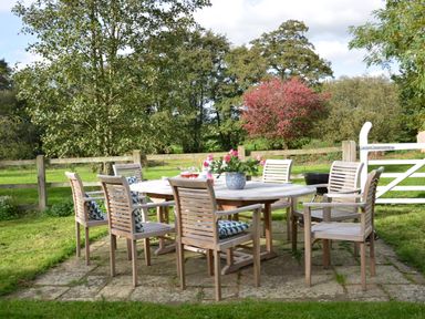 An outdoor dining area with a wooden table and chairs on a stone patio in a fenced garden at Wheelwright's Barn Walpole Near Halesworth