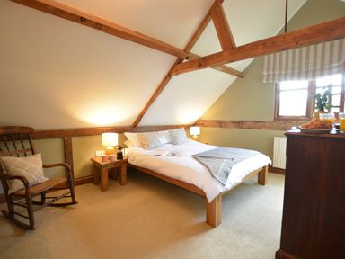 A bedroom with a wooden bed two bedside tables with lamps a wooden rocking chair and a window at Wheelwrights Barn Walpole Near Halesworth