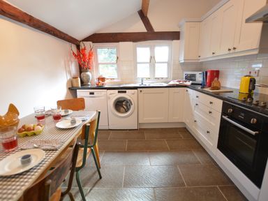 A kitchen with white cabinets a dining table with chairs and flowers on the counter at Wheelwright's Barn in Walpole Near Halesworth