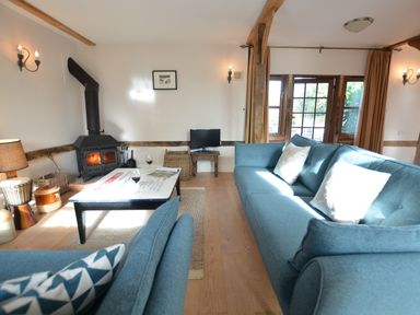 A living room with blue sofas a wood burning stove and a coffee table at Wheelwright's Barn in Walpole Near Halesworth