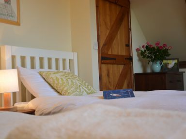 A bedroom with a white bed frame a bedside lamp a wooden door and a dresser with flowers at Wheelwright's Barn Walpole Near Halesworth