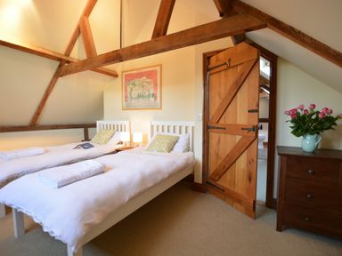 A bedroom with two single beds a wooden door and a chest of drawers with flowers at Wheelwright's Barn Walpole Near Halesworth