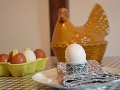 A white egg in an egg cup on a plate with a cloth napkin and a yellow ceramic hen container in the background at Wheelwright's Barn in Walpole Near Halesworth
