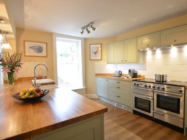 A kitchen with wooden countertops a stainless steel oven a sink with a faucet a bowl of fruit and framed pictures on the walls at Henstead Hall Henstead near Beccles