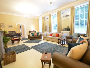 A living room with sofas small tables a piano rugs and large windows at Henstead Hall in Henstead near Beccles