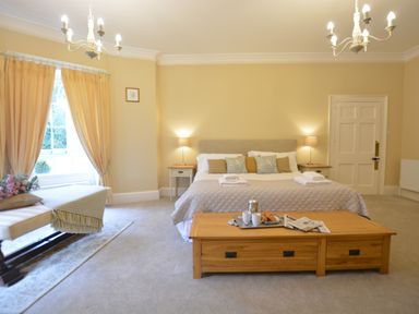 A bedroom with a bed side tables lamps window with curtains bench and a wooden coffee table with breakfast tray at Henstead Hall Henstead near Beccles