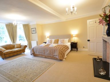 A bedroom with a large bed two bedside tables and lamps a sofa near windows and a rug on the floor at Henstead Hall Henstead near Beccles