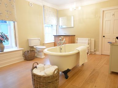 A bathroom with a freestanding bathtub towels in a wicker basket toilet and a vanity unit at Henstead Hall in Henstead near Beccles