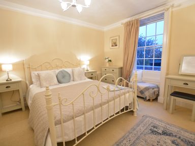 A bedroom with a metal bed frame bedside tables a dresser a window seat and a dressing table at Henstead Hall in Henstead near Beccles