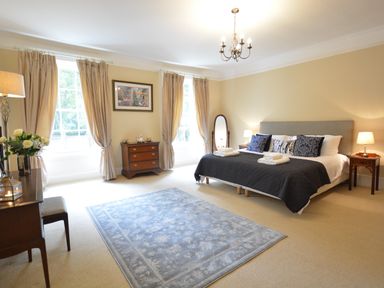 A bedroom with a bed with pillows and towels two bedside tables two windows with curtains a rug and furniture at Henstead Hall in Henstead near Beccles