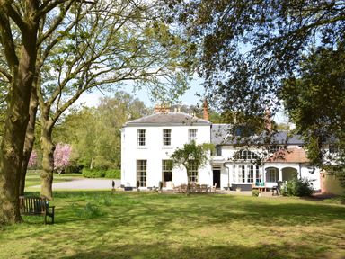 A large white house with outdoor seating on a lawn with trees at Henstead Hall in Henstead near Beccles