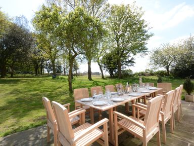An outdoor dining table with wooden chairs set with plates glasses and lanterns in a garden at Henstead Hall in Henstead near Beccles