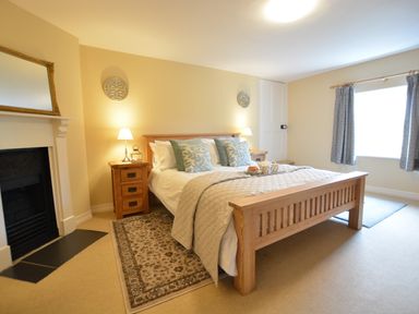 A bedroom with a wooden bed center with pillows bedside tables with lamps and a fireplace at Henstead Hall Henstead near Beccles
