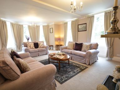 A living room with three sofas a wooden coffee table and curtains at Henstead Hall in Henstead near Beccles