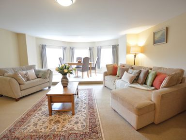 A living room with two beige sofas a wooden coffee table with flowers and a dining area with four chairs and a table at Henstead Hall in Henstead near Beccles