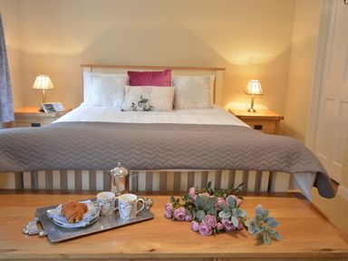 A bedroom with a bed, bedside tables with lamps, a tray with cups and pastries and flowers on a wooden bench at Henstead Hall in Henstead near Beccles