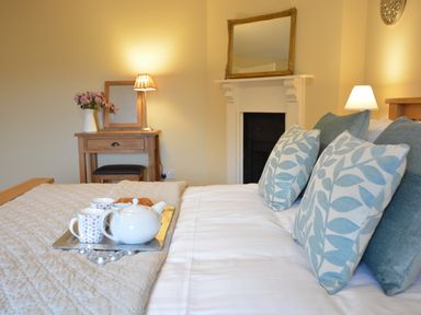 A bedroom with a bed with blue patterned pillows a tray with a teapot and cups a wooden dressing table a lamp and a mirror at Henstead Hall in Henstead near Beccles