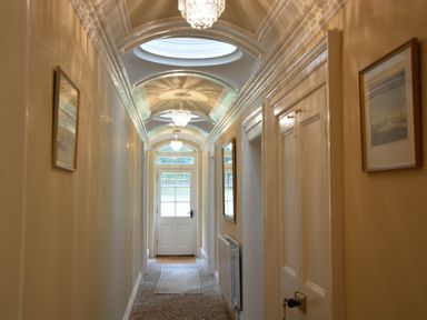 A hallway with chandeliers on the ceiling paintings on the walls and a door at the end at Henstead Hall Henstead near Beccles