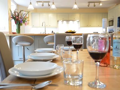 A dining table set with plates glasses and wine glasses in a kitchen with bar stools and flowers at Henstead Hall in Henstead near Beccles