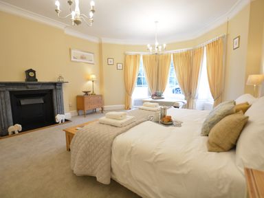 A bedroom with a bed a fireplace a wooden dresser and yellow curtains at Henstead Hall Henstead near Beccles