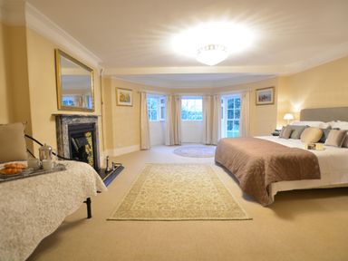 A bedroom with a bed a fireplace and large windows at Henstead Hall in Henstead near Beccles