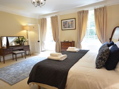 A bedroom with a bed a dresser with a mirror and flowers and a chest of drawers with a tea set at Henstead Hall in Henstead near Beccles