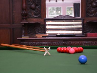 A snooker table with cues, a triangle of red balls, a pink ball, and a blue ball in a room with wooden paneling at Henstead Hall Henstead near Beccles