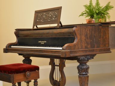 An antique wooden piano with carved legs and a red cushioned bench a fern plant on top of the piano at Henstead Hall in Henstead near Beccles