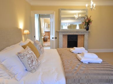 A bedroom with a bed pillows folded towels a fireplace with a mirror and flowers at Henstead Hall Henstead near Beccles