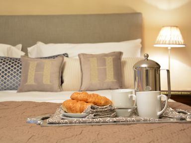A bed with pillows and a breakfast tray holding croissants cups and a coffee pot at Henstead Hall in Henstead near Beccles