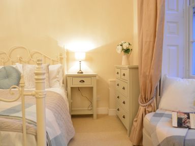 A bedroom with a bed side table lamp chest of drawers and a chair with a book at Henstead Hall Henstead near Beccles