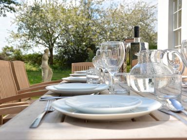An outdoor wooden dining table set with plates glasses cutlery and a water jug with trees and a statue in the background at Henstead Hall Henstead near Beccles