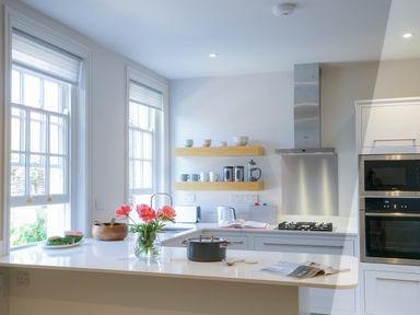 A kitchen with two large windows flowers on the counter and floating shelves holding mugs and jars at 10 Church Walk Aldeburgh