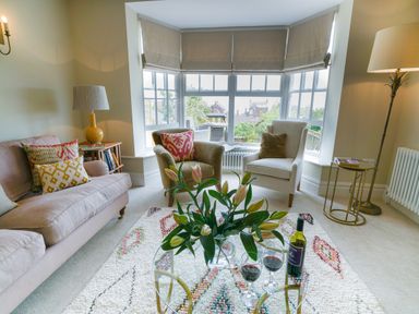 A living room with two armchairs and a sofa around a glass coffee table with flowers and wine at 10 Church Walk Aldeburgh