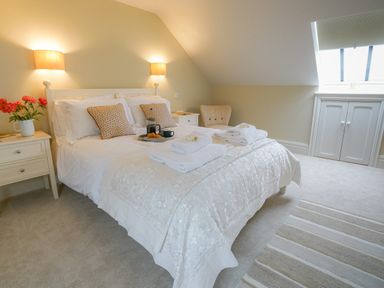 A bedroom with a bed, bedside tables with lamps, a chair, and a window at 10 Church Walk, Aldeburgh