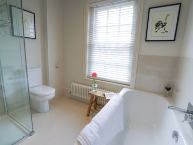 A bathroom with a bathtub a shower a toilet a wooden stool with a flower and a book at 10 Church Walk Aldeburgh