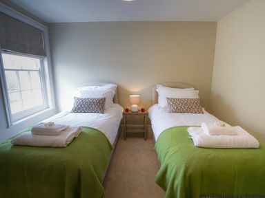A bedroom with two single beds with green blankets and white towels with a lamp on a wooden side table between the beds at 10 Church Walk Aldeburgh