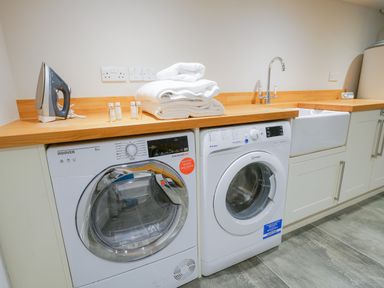 A laundry room with a Hoover dryer, Indesit washing machine, sink, iron, towels, and toiletries at 10 Church Walk Aldeburgh