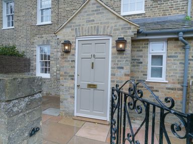 A front door with the number 10 on a brick house with two outdoor wall lights and a black wrought iron gate at 10 Church Walk Aldeburgh