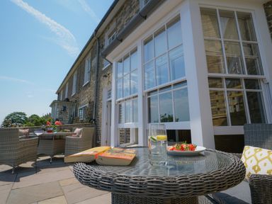 An outdoor patio with wicker furniture and a glass table holding books a glass of water and a plate of strawberries at 10 Church Walk Aldeburgh