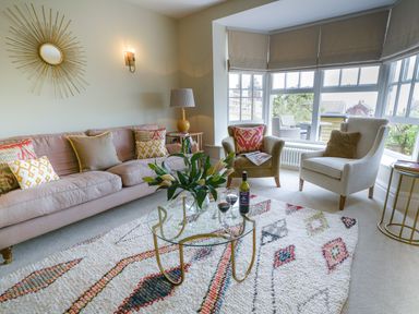 A living room with a sofa armchairs a glass coffee table and large windows at 10 Church Walk Aldeburgh