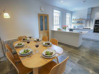 A dining area with a wooden table set with plates of salad and glasses of red wine next to a kitchen with white cabinets and an island at 10 Church Walk  Aldeburgh