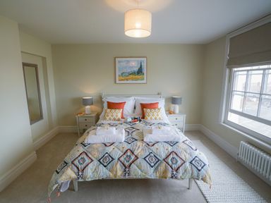 A bedroom with a bed side tables lamps and a window at 10 Church Walk Aldeburgh